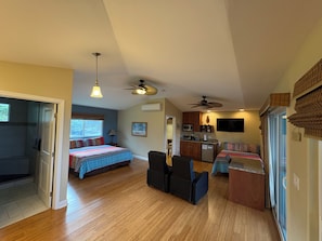 A compact living space with a kitchenette, a bed with patterned bedding, a dining area with chairs, and a ceiling fan.