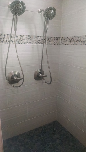 A shower with two handheld showerheads and a control knob.