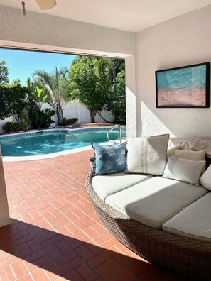 Relax by the pool surrounded by lush greenery and a wicker sofa.