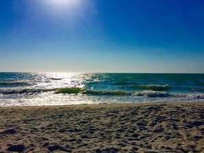 Ein Strand mit Sand und Wellen unter blauem Himmel.
