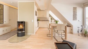 A modern kitchen with a central stove, a dining area with a table and chairs, and a visible staircase leading to an upper level. - Villa Allegra - 2-room-App. for 1-4 persons (20) - Villa Allegra (Binz)