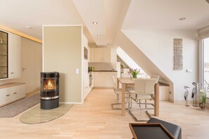 Una cocina moderna con estufa central, zona de comedor con mesa y sillas, y una escalera visible que conduce a un nivel superior.