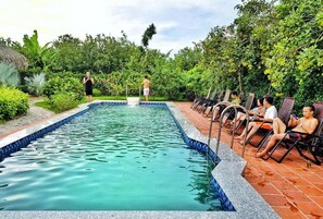 A swimming pool with a tiled edge, surrounded by lush greenery and a brick patio.