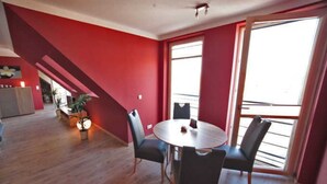 A modern apartment with a red accent wall, a dining area with a round table and four chairs, and a kitchen in the background.