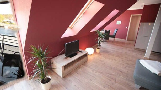 A modern living room with a TV on a wooden console, a dining area with chairs, and a potted plant.