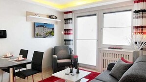 Ein modernes Wohnzimmer mit einer Couch, einem Esstisch mit Stühlen, einem Couchtisch, einem Kamin und einem großen Fenster mit Vorhängen.