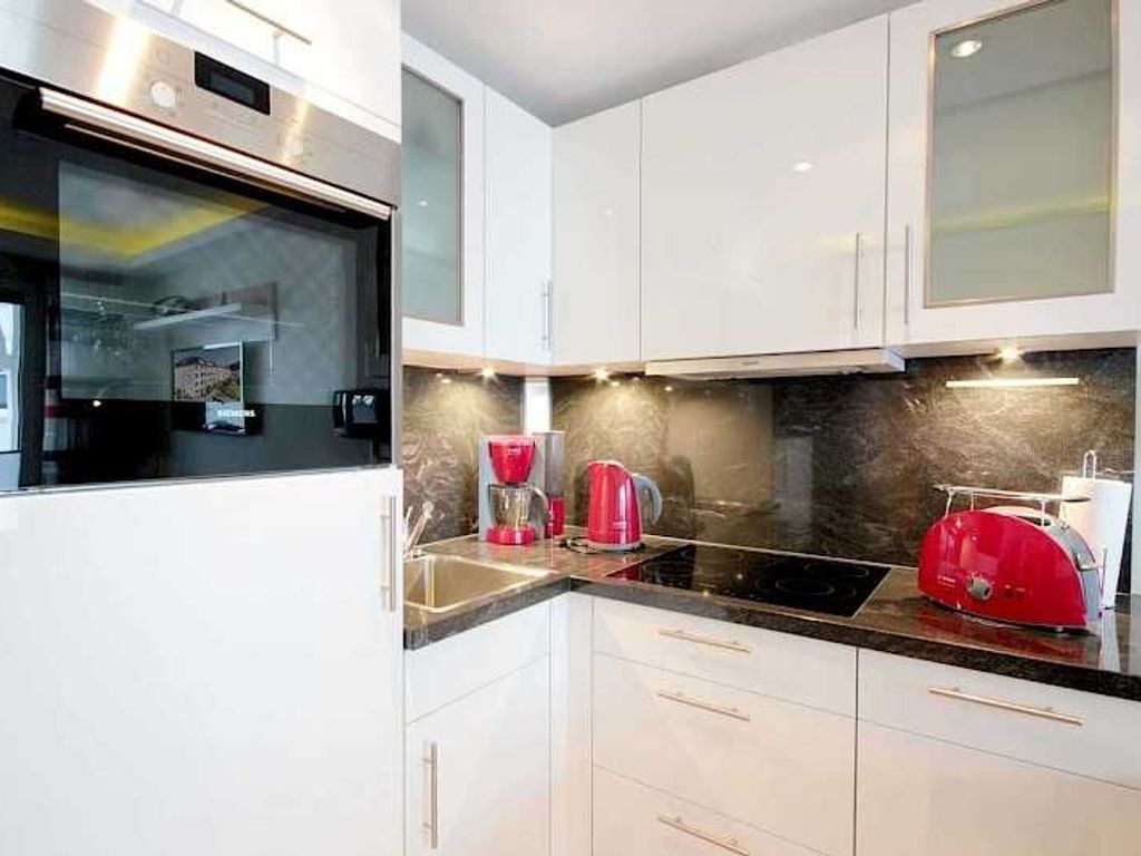 A modern kitchen with white cabinets, a black countertop, and a red appliance.