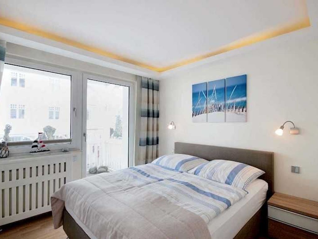 A bedroom with a bed, a window, a radiator, and a wall-mounted artwork.
