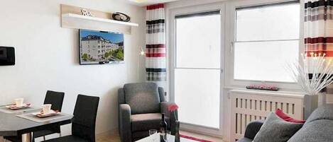 Una sala moderna con sofá, mesa de comedor con sillas, mesa de centro, chimenea y un amplio ventanal con cortinas.