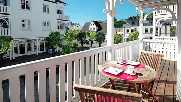 Ein Balkon mit Tisch und Stühlen, weißen Geländern und Blick auf die umliegenden Gebäude.