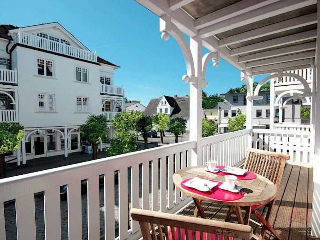 Ein Balkon mit Tisch und Stühlen, weißen Geländern und Blick auf die umliegenden Gebäude.