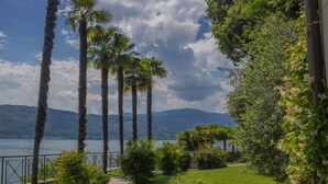 Ein Garten mit Palmen, einem Weg und Blick auf einen See und Berge.