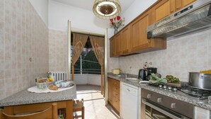 Eine Küche mit Herd, Backofen und Geschirrspüler. Ein Fenster mit Vorhängen, ein Spülbecken und eine Arbeitsplatte mit verschiedenen Gegenständen.