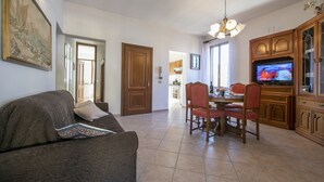 Ein Wohnzimmer mit einer Couch, einem Esstisch mit Stühlen, einem Fernseher und Holzschränken.