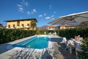 A swimming pool with a clear blue water, surrounded by a patio area with chairs and an umbrella.