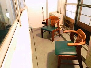 A narrow hallway with two wooden chairs with green cushions, a white heater, and a window with blinds. - Matsuki building Seaside Mansion (Beppu)