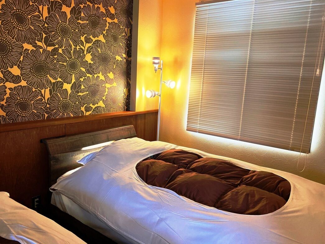 Una cama individual con cabecera, una lámpara de pared y una ventana con persianas.