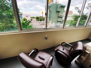 A room with two brown leather chairs, a window with a view of a street, and a small trash bin on the floor. - Matsuki building Seaside Mansion (Beppu)