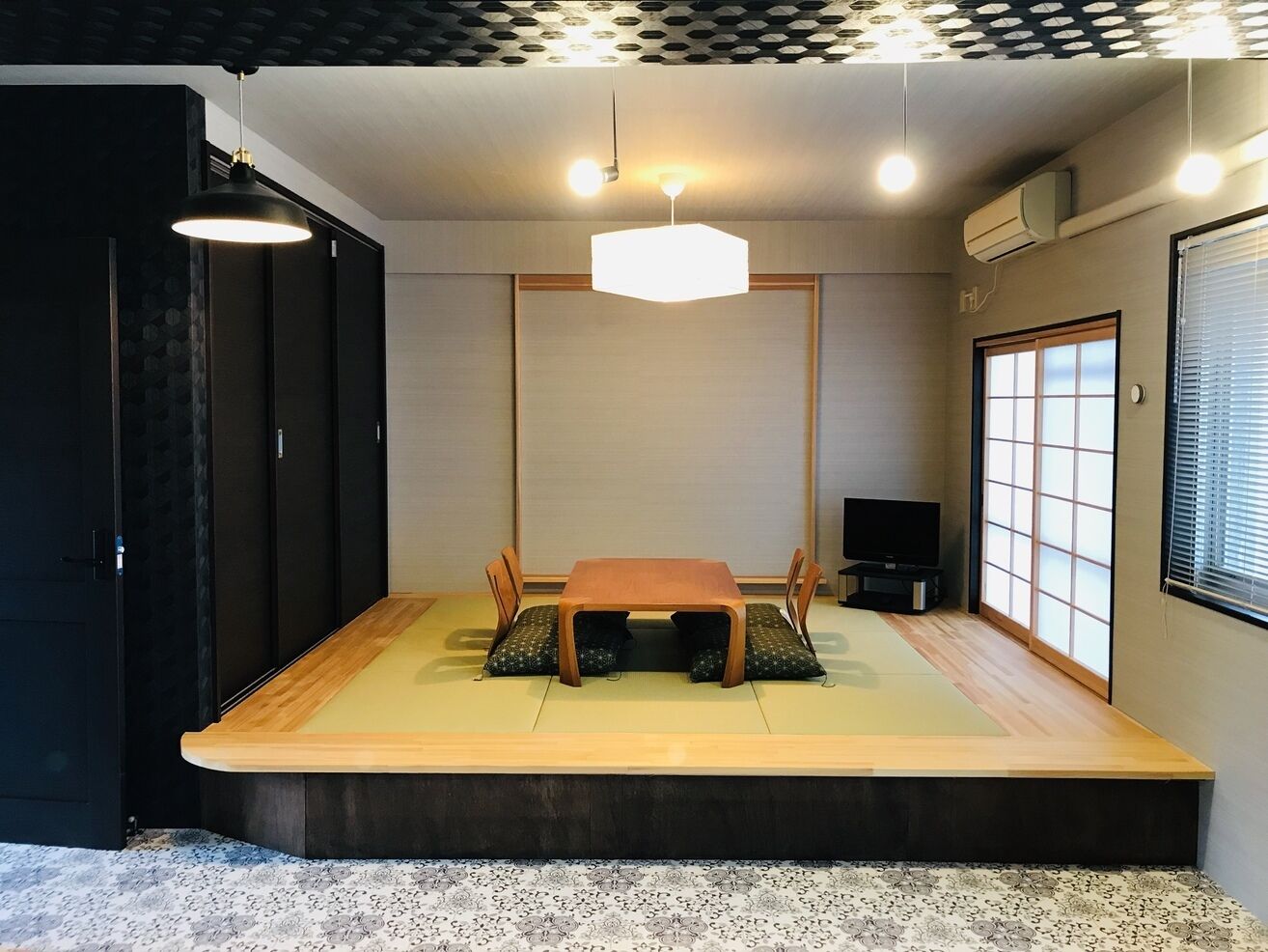 A traditional Japanese tatami room with a low table, tatami mats, a sliding door, and a television.