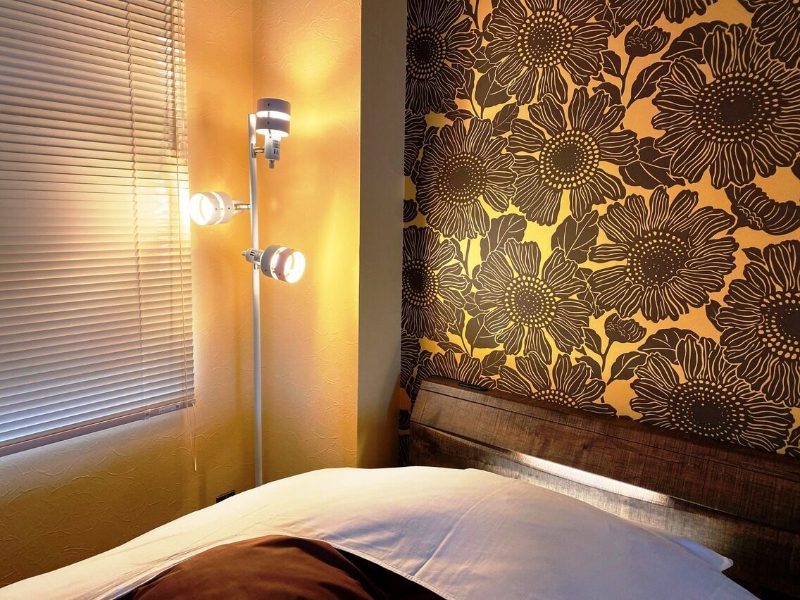 Una habitación con una cama, una lámpara de pared y un estampado floral en el papel tapiz.