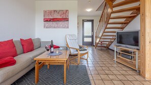 A living room with a sofa, a coffee table, a TV on a wooden stand, a chair, and a staircase. - La Casa vacation apartment Kormoran - Holiday apartment Kormoran (Steinberg)