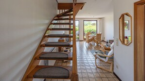 A staircase with wooden steps and cushioned seats, leading to a room with a dining table and chairs, a mirror, and a view of greenery outside. - La Casa vacation apartment Kormoran - Holiday apartment Kormoran (Steinberg)