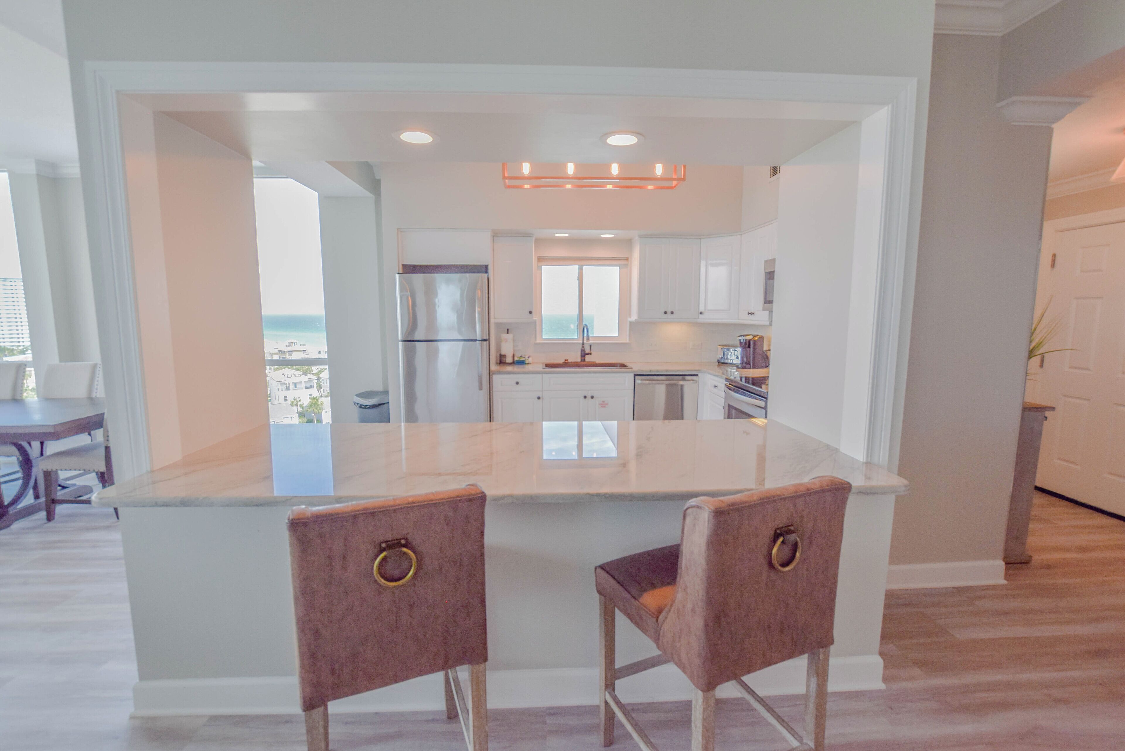 A modern kitchen with a large island, two barstools, and a view of the ocean.