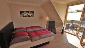 A bedroom with a bed, a chair, a lamp, and a balcony with a view. - Apartment 7 - Holiday apartments Jack & Richies (Greifswald)