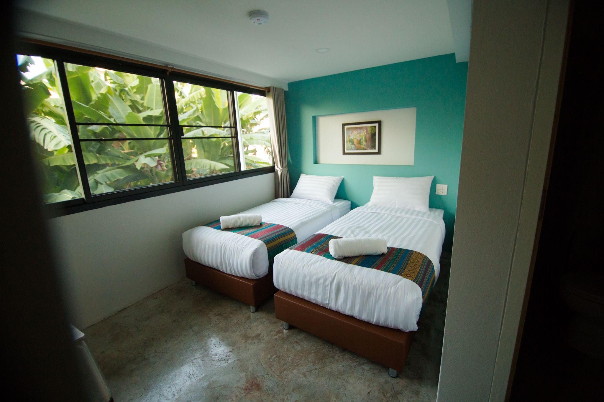 Una habitación con dos camas individuales, una ventana con vistas a zonas verdes y una pared color turquesa.