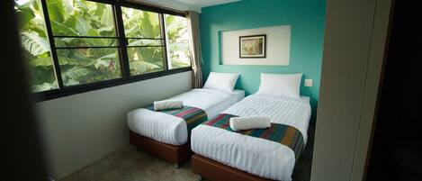Una habitación con dos camas individuales, una ventana con vistas a zonas verdes y una pared color turquesa.