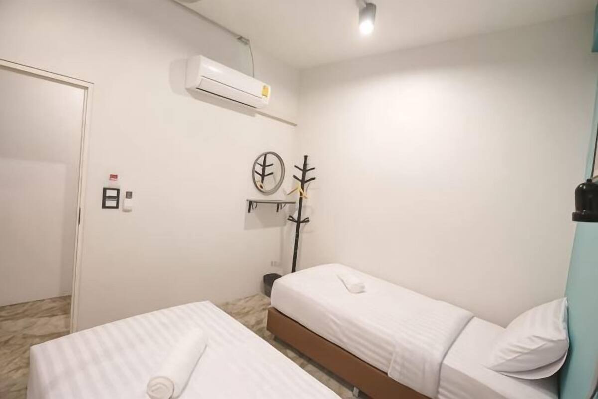 A room with two beds, a door, an air conditioning unit, a coat rack, and a clock on the wall.