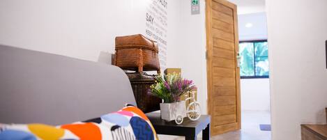 A modern interior with a grey sofa, a small table with a basket and flowers, and a wooden door leading to another room.