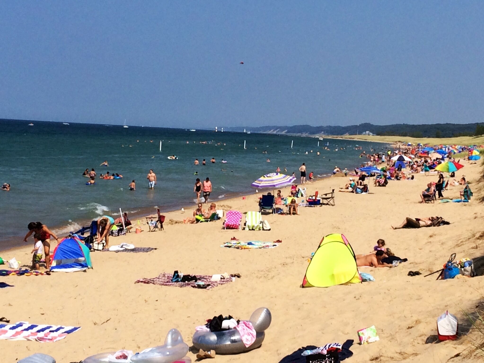 Una playa concurrida donde gente se toma el sol, nada y juega.
