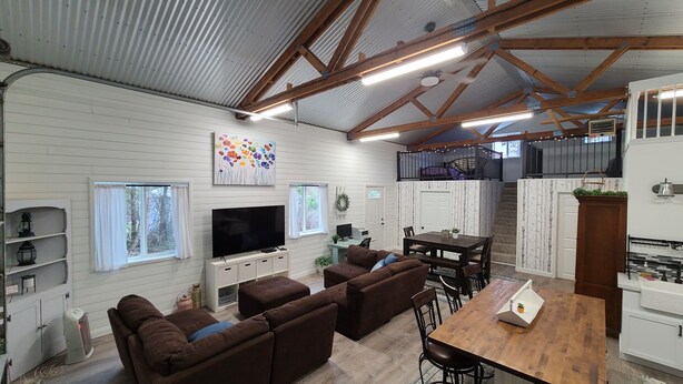 A spacious living area with a large TV, brown sofas, a wooden dining table, and a kitchen area with a balcony. - Included RV Spot + 10 min to Silverwood  (Hayden)