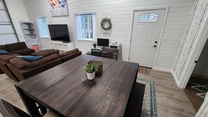 A living room with a brown sofa, a wooden dining table with a potted plant, a TV, and a door with a wreath. - Included RV Spot + 10 min to Silverwood  (Hayden)