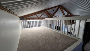 An attic space with a sloped ceiling, wooden beams, and a white railing. - Included RV Spot + 10 min to Silverwood  (Hayden)