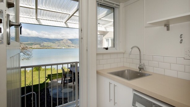 A kitchen with a view of a lake, a balcony with a table and chairs, and a dishwashing machine.
