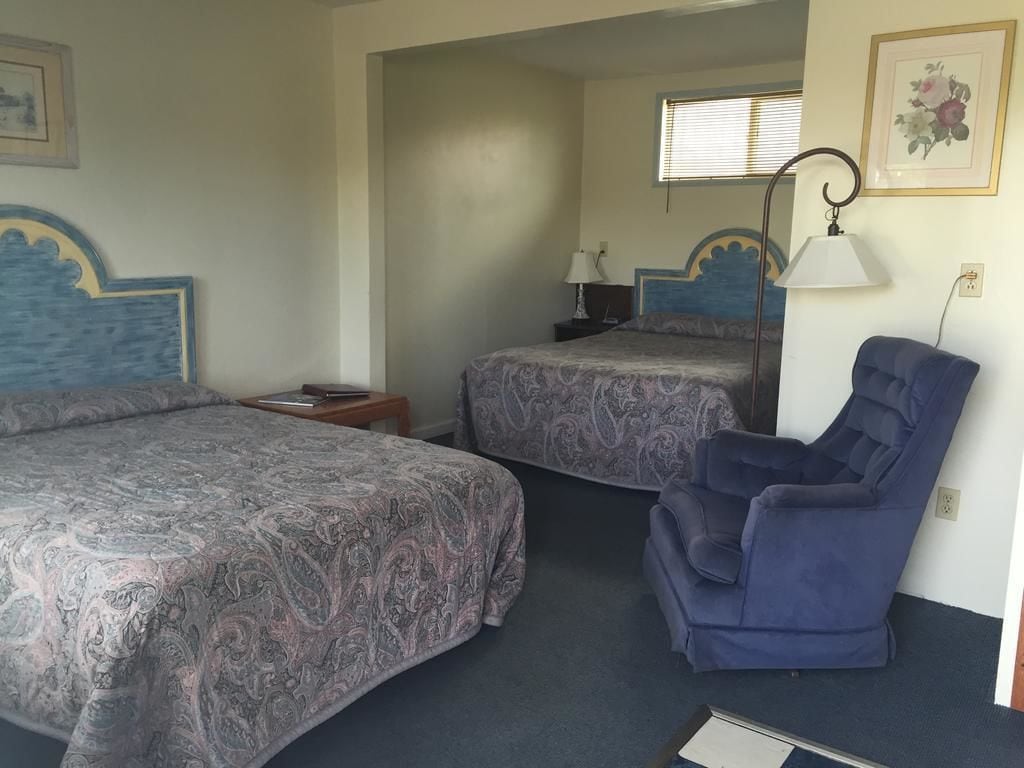 Ein Schlafzimmer mit zwei Betten, einem blauen Sessel, einem Nachttisch und einer Lampe.
