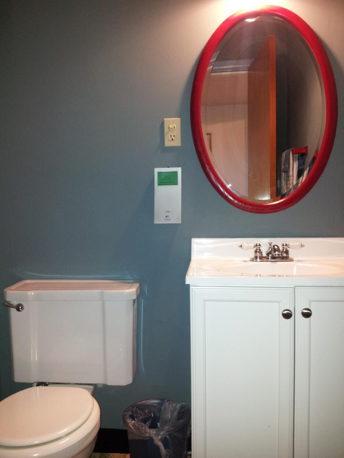 Un baño con inodoro, lavamanos con espejo y un cubo de basura.