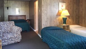 Une chambre avec deux lits, un fauteuil à motifs, une table de chevet avec une lampe et un tableau encadré au mur.