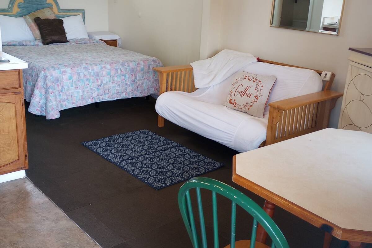 A room with two beds, a wooden chair, a table, and a mirror.
