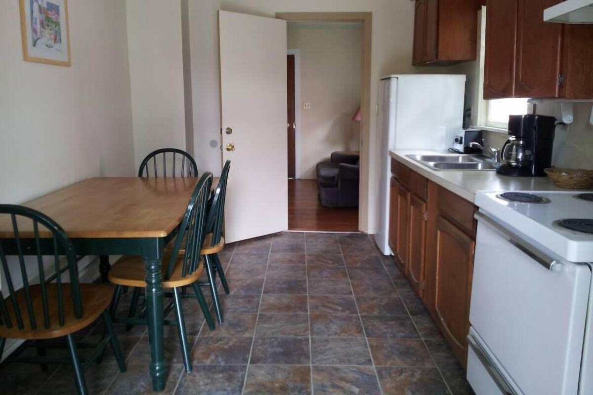 A kitchen with a dining table and chairs, a refrigerator, and a coffee maker.
