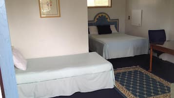 A small, simple room with two single beds, a small table, and a chair.