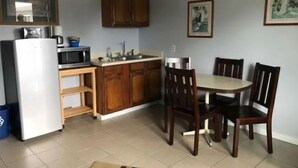 Une cuisine compacte avec des meubles en bois, un réfrigérateur blanc, un four à micro-ondes et un évier. On y trouve une table à manger avec quatre chaises.