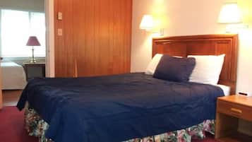 A neatly made bed with a blue bedspread and floral skirt, two bedside lamps, and a wooden headboard in a hotel room.