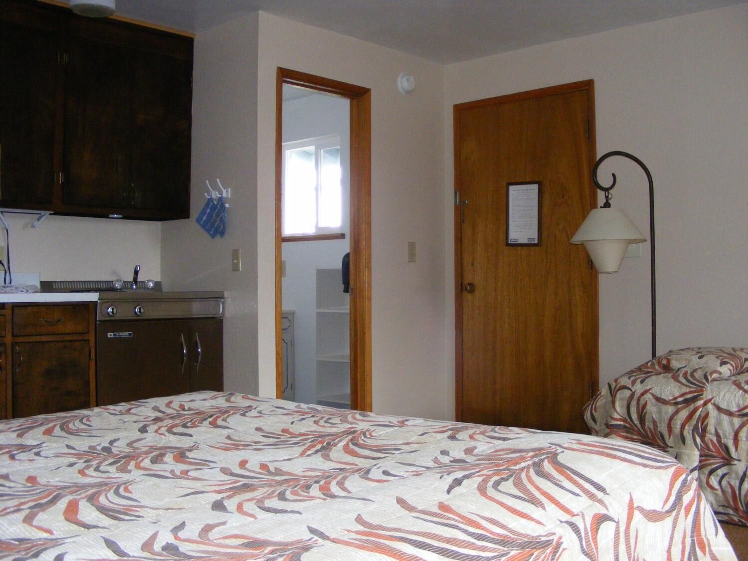 Un dormitorio con cama, armario de madera, espejo y puerta.