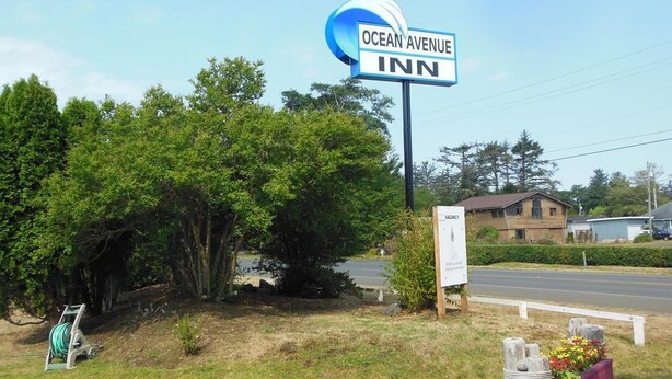 Une enseigne pour l’hôtel Ocean Avenue Inn, un panneau publicitaire vide et un espace paysager agrémenté d’un jardinier.