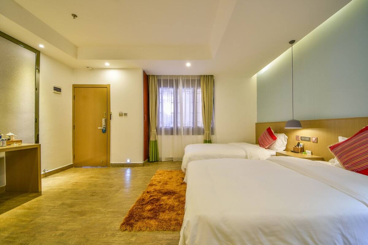 A hotel room with two beds, a desk, a small bathroom, and a window with curtains.