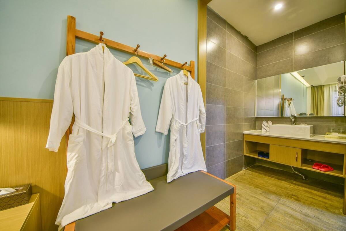 A bathroom with a wooden bench, a mirror, and two white robes hanging on a rack.