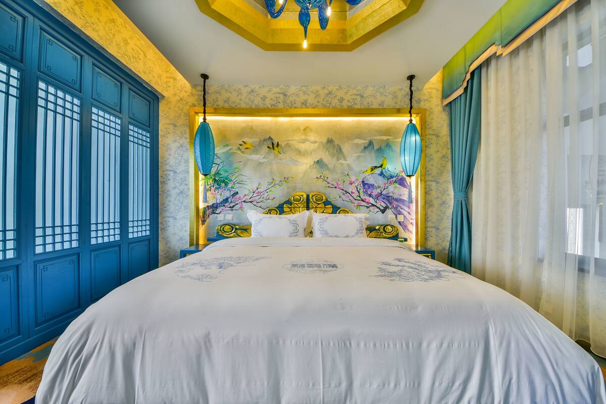 Un dormitorio con una cama grande, armarios azules, un mural decorativo y lámparas azules colgantes.